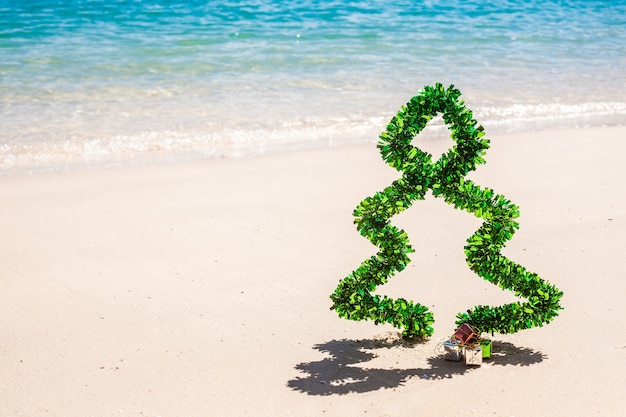 Albero di Natale di tinsel sulla spiaggia con sabbia bianca e acqua blu