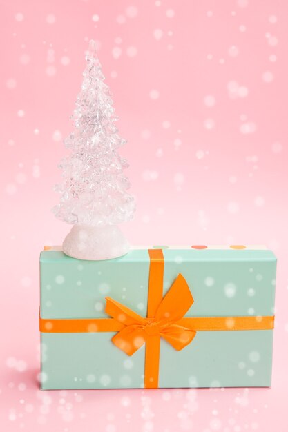 Albero di Natale di vetro su una scatola verde con un fiocco arancione su sfondo rosa