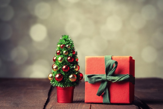 Albero di Natale e scatola regalo rossa sul tavolo di legno con bokeh sullo sfondo