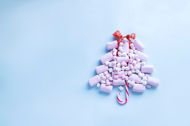 Albero di Natale fatto di marshmallow rosa e bastoncino di zucchero su sfondo azzurro