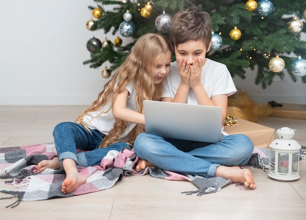 Albero di Natale in un ampio soggiorno. I bambini giocano vicino all'albero di Natale. Un ragazzo con un laptop comunica con gli amici.