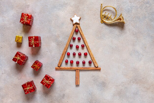 Albero di Natale originale fatto con bastoncini di cannella, bacche rosse e biscotti a forma di stella con regali e tromba