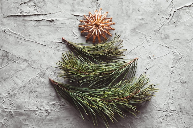 Albero di Natale realizzato con foglie di pino e giocattoli di paglia. su uno sfondo grigio cemento.