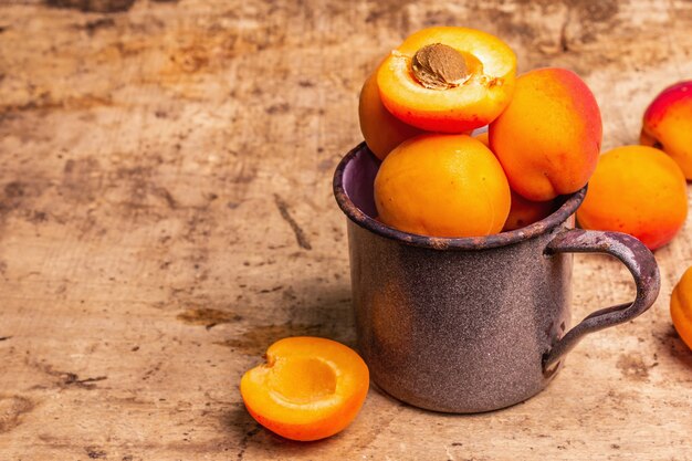 Albicocche mature in una tazza di ferro vintage. Frutti dolci, vecchio tavolo in legno, copia spazio