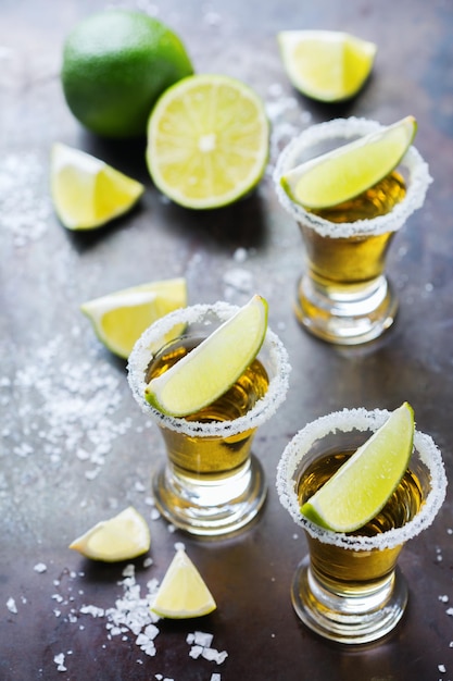 Alcol cibo spazzatura festa concetto di tequila messicana dorata sparata su un tavolo nero grunge con sale e lime