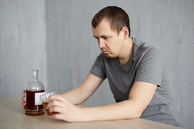 Alcolismo e concetto di depressione - giovane infelice seduto con bicchiere e bottiglia di whisky a casa o al pub