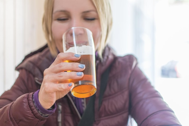 Alcolismo femminile Una donna in giacca beve birra da un bicchiere in un caffè di strada