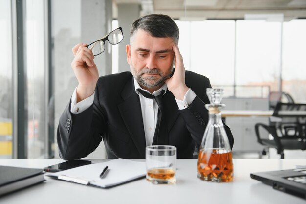 Alcolismo sul lavoro Dipendente stanco che beve alcol sul posto di lavoro non può gestire lo stress