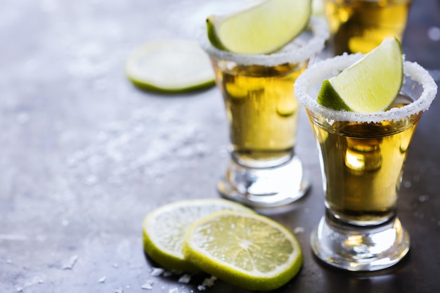 Alcool cibo spazzatura festa concetto di tequila messicana dorata girato su un tavolo nero grunge con sale e calce copia spazio sullo sfondo