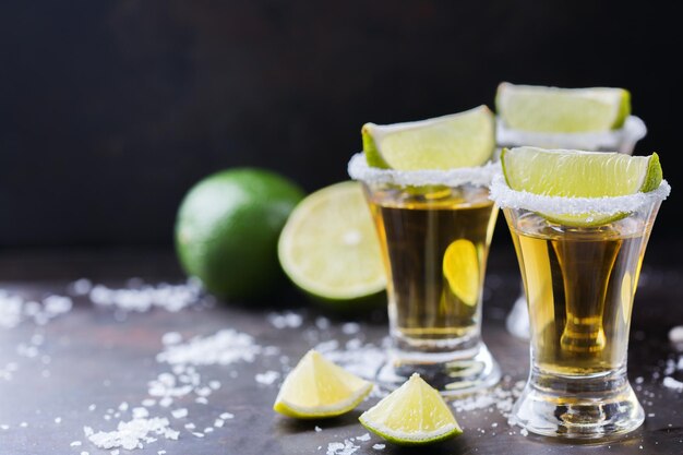 Alcool cibo spazzatura festa concetto di tequila messicana dorata girato su un tavolo nero grunge con sale e calce copia spazio sullo sfondo