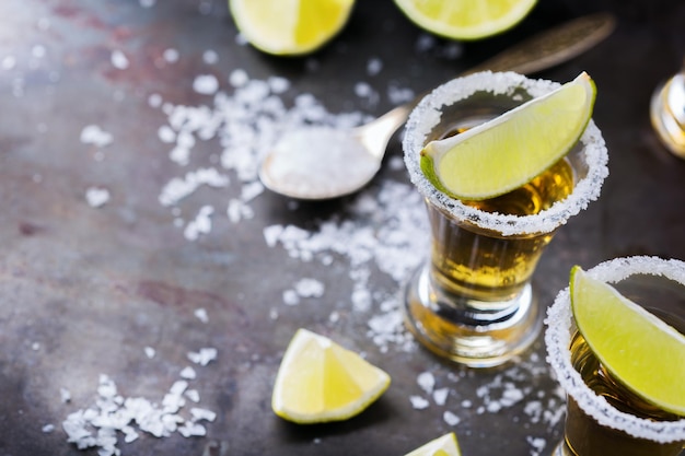 Alcool cibo spazzatura festa concetto di tequila messicana dorata girato su un tavolo nero grunge con sale e calce copia spazio sullo sfondo