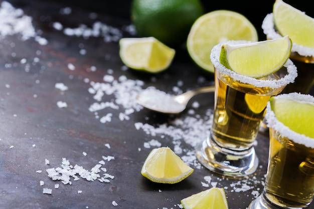 Alcool cibo spazzatura festa concetto di tequila messicana dorata girato su un tavolo nero grunge con sale e calce copia spazio sullo sfondo