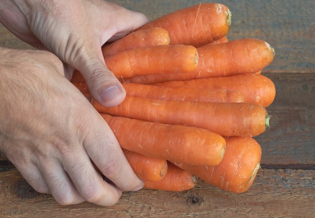 Alcune carote dolci nella mano di un uomo I benefici del concetto di carote Fondo in legno