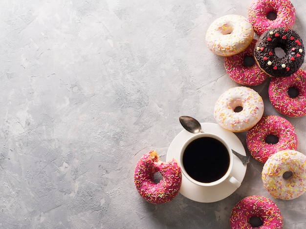 Alcune ciambelle rosa e bianche con una tazza di caffè su struttura di pietra grigia, vista dall'alto, copia dello spazio