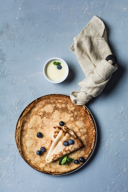 Alcune frittelle in padella con mirtilli e menta, con latte dolce condensato in una salsiera