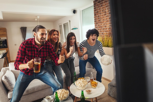 Alcuni amici, appassionati di sport, amano trascorrere il loro tempo libero a casa insieme guardando la partita di calcio alla TV. Stanno urlando e indicando una vittoria.