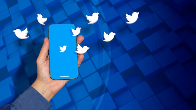 Alcuni loghi di Twitter che emergono da uno smartphone su una mano maschile su uno sfondo blu su uno sfondo blu