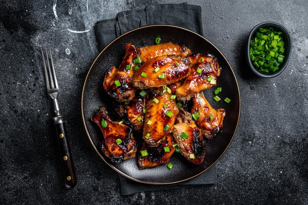 Alette di pollo al forno con salsa di peperoncino dolce in un piatto sfondo nero vista dall'alto