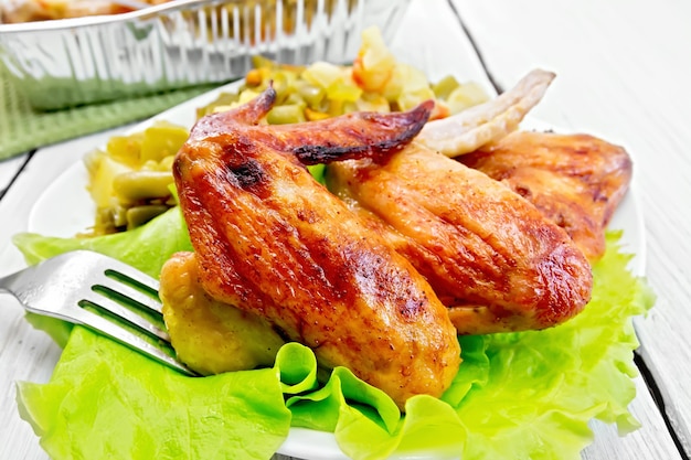 Alette di pollo fritte con verdure e foglie di insalata su un piatto, forchetta su tavole di legno chiaro di sfondo