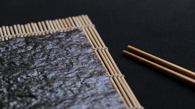 Alghe nori sopra un makisu, tappetino di bambù con bacchette su sfondo nero