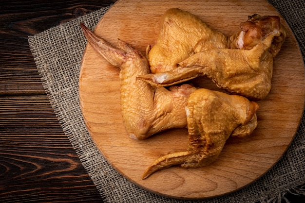 Ali di pollo affumicate sulla tavola di legno su fondo di legno scuro.