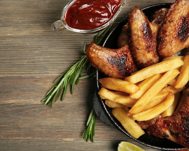 Ali di pollo al forno con patatine fritte su un tavolo di legno