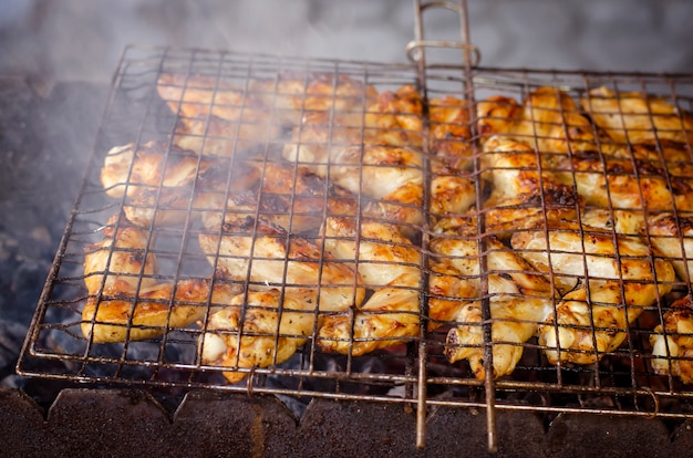 Ali di pollo alla griglia su una griglia con il fumo per la festa del cortile.