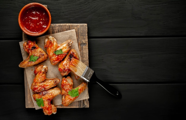 Ali di pollo arrostite con salsa barbecue con prezzemolo su un tagliere su fondo di legno