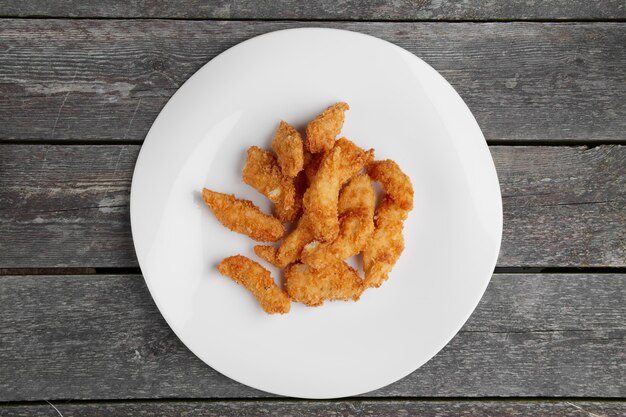 Ali di pollo arrostite croccanti su un piatto bianco sulla tavola di legno, vista superiore.