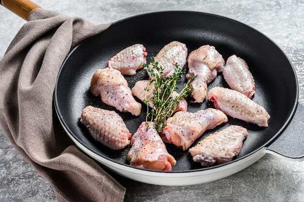 Ali di pollo con spezie ed erbe pronte da cucinare in padella. Sfondo grigio.