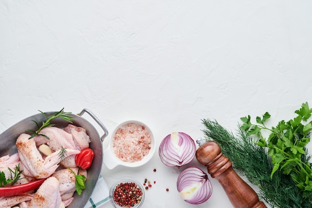 Ali di pollo crude in una ciotola bianca con spezie e ingredienti per cucinare su sfondo chiaro di ardesia, pietra o cemento. Vista dall'alto con copia spazio. Modello.