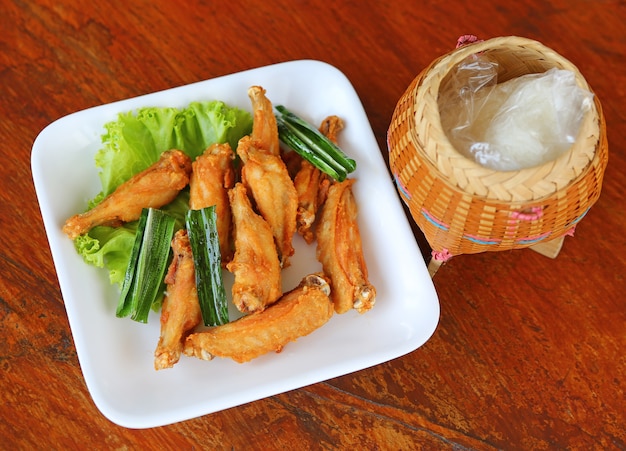 Ali di pollo fritto in un piatto bianco con riso appiccicoso in scatola di bambù