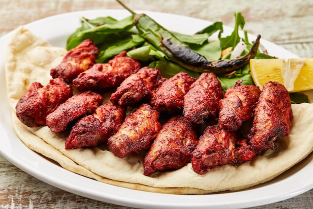 Ali di pollo piccanti con fetta di limone e insalata servite in un piatto isolato sul tavolo vista del cibo arabo