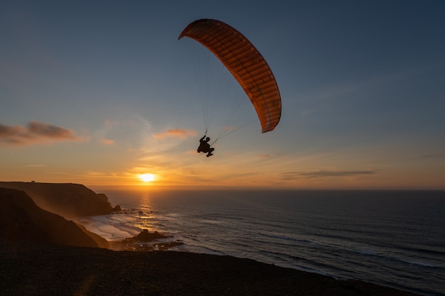 Aliante che sorvola la riva di mare al tramonto. Sport in parapendio