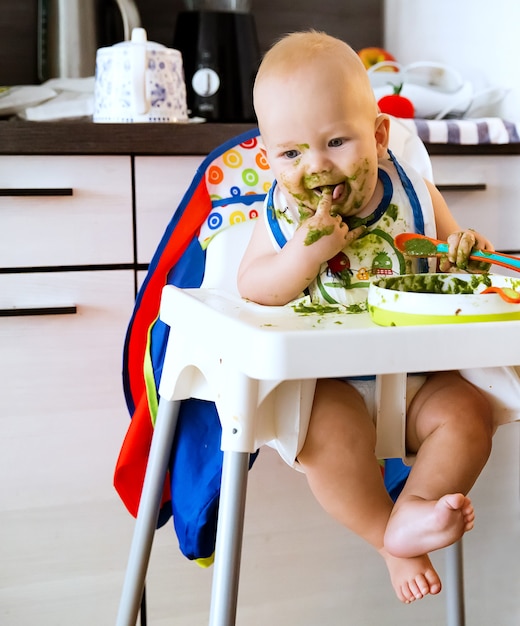 Alimentazione Adorabile bambino che mangia con un cucchiaio nel seggiolone Il primo cibo solido del bambino