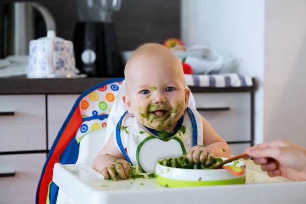 Alimentazione. Adorabile bambino che mangia con un cucchiaio nel seggiolone. Il primo cibo solido del bambino