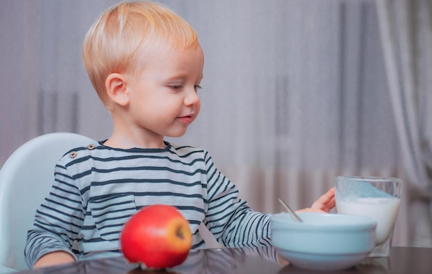 Alimentazione del bambino Mangiare sano Bambino che fa spuntino Bere latte Bambino tenere un bicchiere di latte Bambino ragazzo carino sedersi a tavola con piatto e cibo Cibo sano Alimentazione sana Ragazzo bambino carino mangiare colazione