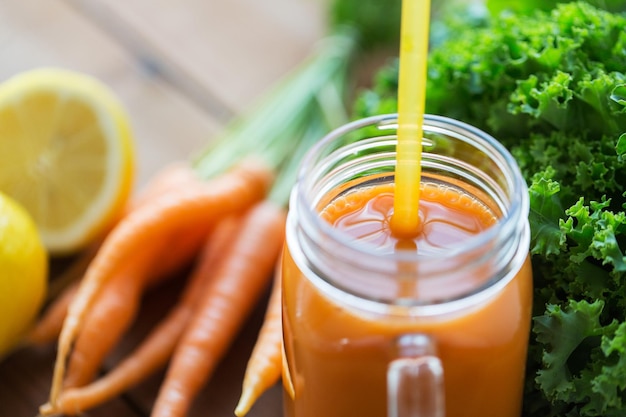 alimentazione sana, cibo, dieta e concetto vegetariano - primo piano di caraffa di vetro o tazza con succo di carota, frutta e verdura su tavola di legno