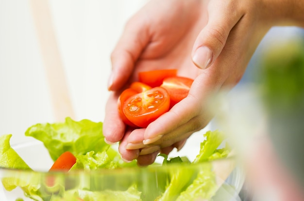 alimentazione sana, cibo vegetariano, dieta e concetto di persone - primo piano di una giovane donna che cucina insalata di verdure e aggiunge pomodori a casa