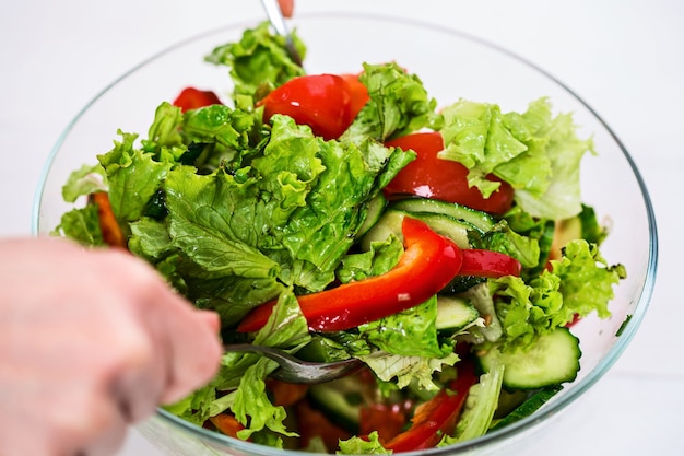 Alimentazione sana, cibo vegetariano, dieta e concetto di persone - primo piano di una giovane donna che veste insalata di verdure con olio d'oliva su sfondo bianco