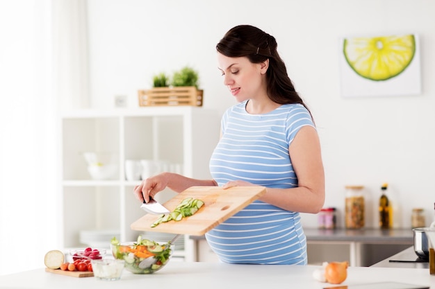 Alimentazione sana, gravidanza e concetto di persone - donna incinta che cucina insalata di verdure a casa cucina