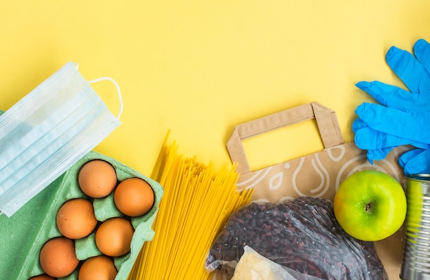 Alimenti base e maschera chirurgica, vista dall'alto. Concetto di generi alimentari e coronavirus