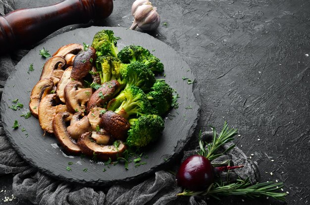 Alimenti biologici Funghi e broccoli fritti su una lastra di pietra nera Stile rustico Vista dall'alto