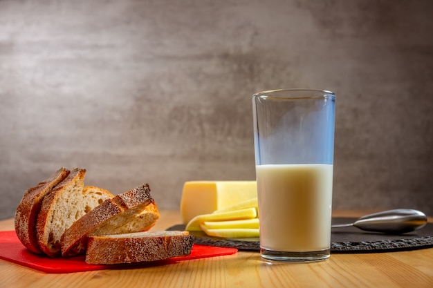 Alimenti biologici su un tavolo di legno. Fette di formaggio fresco, pane e un bicchiere di latte