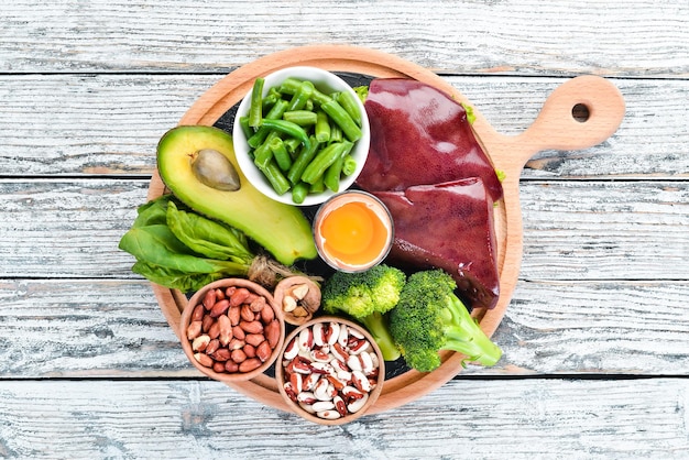 Alimenti che contengono vitamina B9 naturale Fegato avocado broccoli spinaci fagioli prezzemolo noci su fondo di legno bianco Vista dall'alto