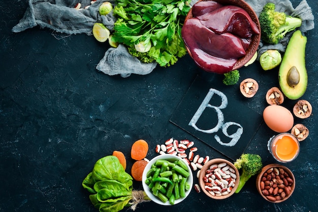 Alimenti che contengono vitamina B9 naturale Fegato avocado broccoli spinaci fagioli prezzemolo noci su sfondo di pietra nera Vista dall'alto