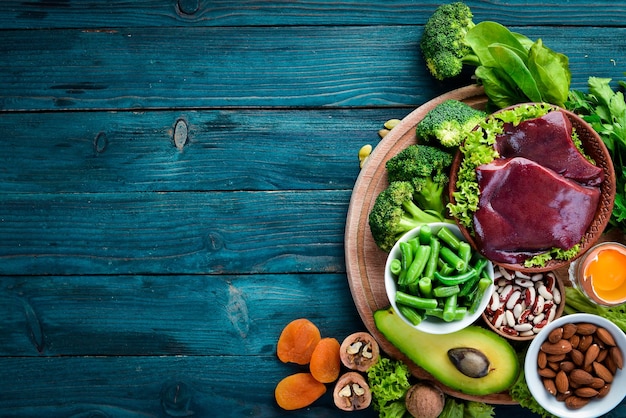 Alimenti contenenti ferro naturale Fe Fegato avocado broccoli spinaci prezzemolo fagioli noci su sfondo blu Vista dall'alto