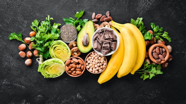 Alimenti contenenti magnesio naturale Mg Cioccolato banana noci di cacao avocado broccoli mandorle Vista dall'alto su sfondo nero