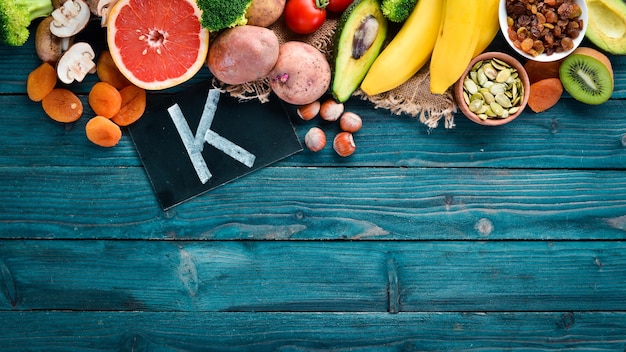 Alimenti contenenti potassio naturale K Patate funghi banana pomodori noci fagioli broccoli avocado Vista dall'alto su sfondo di legno blu