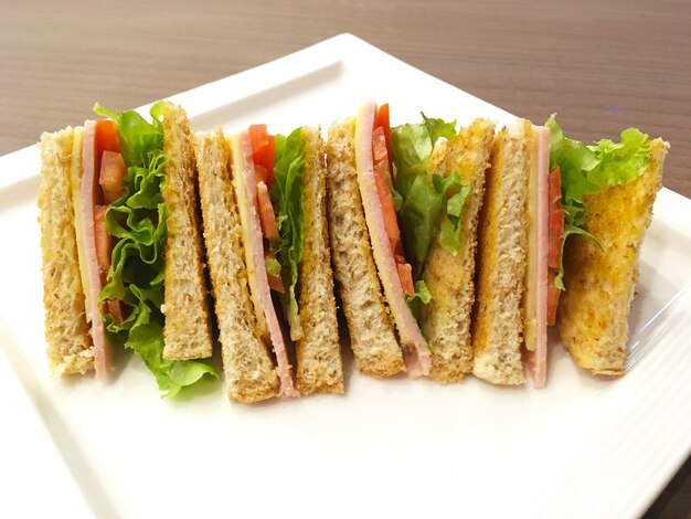 Alimenti dietetici per la colazione. Pane integrale del panino con lattuga, prosciutto e formaggio giallo sulla zolla bianca sopra la tavola di legno di mattina.